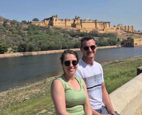 Couple posing beside a tranquil moat with the massive yellow sandstone Amber Fort rising on the hill behind.