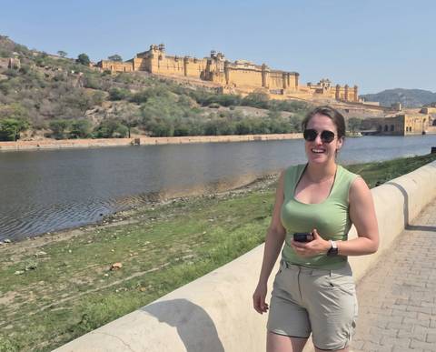 Female traveler smiling beside a stone balustrade overlooking the lake and towering Amber Fort in Rajasthan.