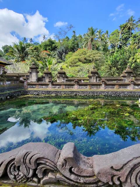 Sacred spring pool reflecting temple walls, lush trees and sky in Bali.