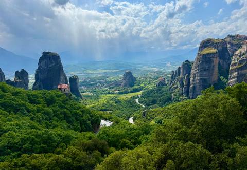 Panoramic vista of lush Meteora rock pillars and monasteries under dramatic sky.