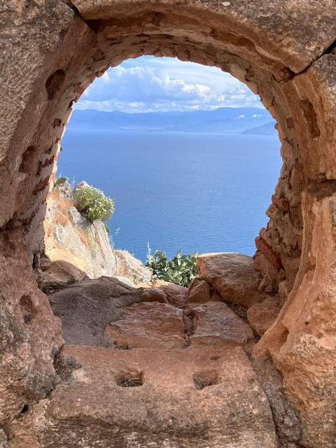 Rocky window frame overlooking deep blue Aegean sea and rugged coastline.