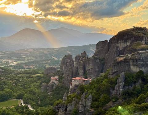 Dramatic sunray breaking through clouds above Meteora's rocky pinnacles and monastery.