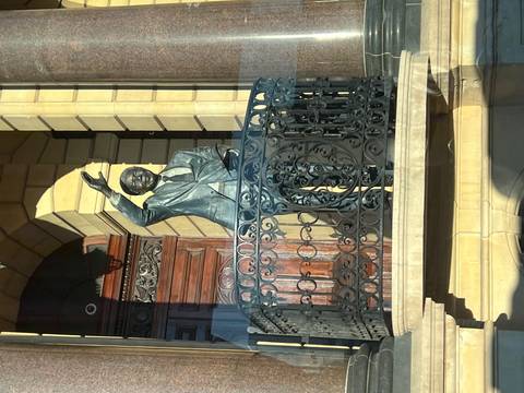 Bronze statue of Nelson Mandela waving from an ornate balcony in front of a historic building