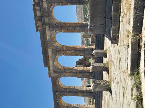 Stone arches and columns of the ancient Roman ruins at Volubilis rise against a bright blue sky.