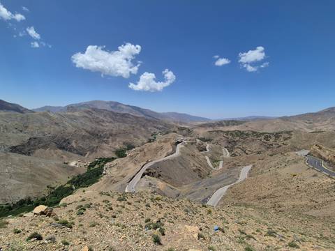 Wide panoramic view of winding mountain road snaking through the rugged Atlas landscape under a lone cloud.