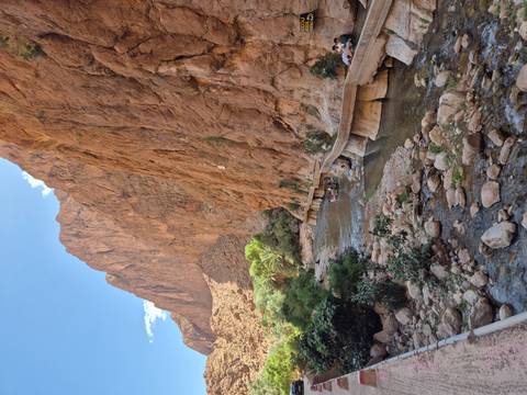 Narrow stream flowing through the dramatic red cliffs of Todra Gorge with a stone walkway beside it.