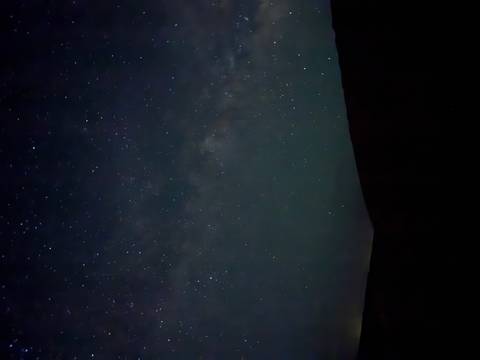 Star-filled night sky with faint Milky Way above a dark desert horizon.