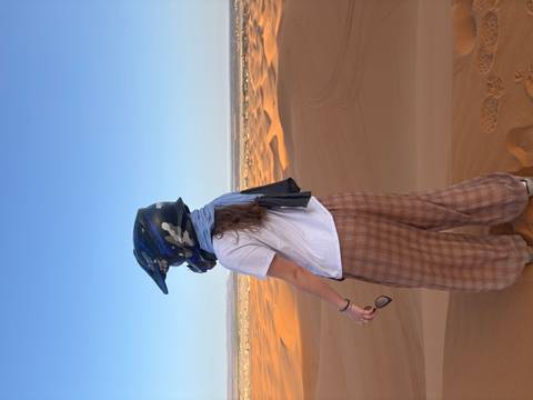 Woman wearing an ATV helmet gazes over vast rolling dunes from a high vantage point.