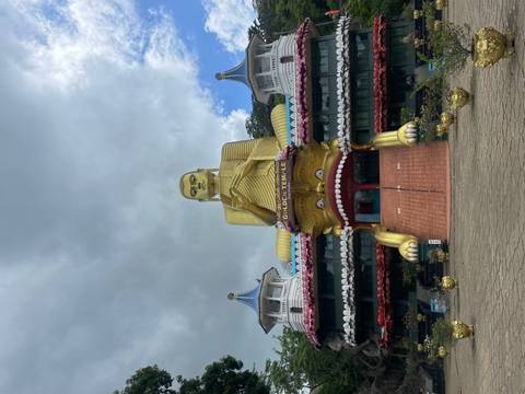 The towering golden Buddha statue at Dambulla Golden Temple rises against a dramatic cloudy sky.