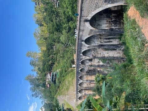 The historic Nine Arches Bridge spans a lush green valley with bright blue skies overhead.