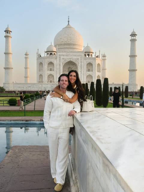 A smiling couple embraces in front of the Taj Mahal at dusk, its white marble glowing softly.