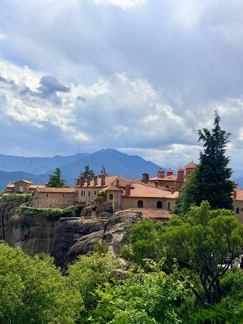 A hilltop monastery with terracotta roofs stands against a backdrop of distant blue mountains.