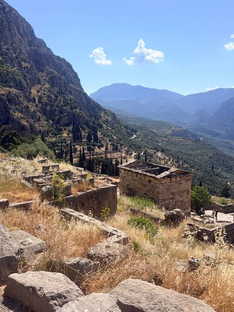 Ruins of ancient Delphi cascade down a sun-drenched mountain slope with olive groves below.