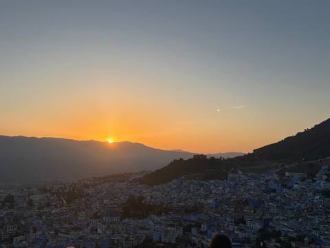 Golden sun sets behind mountains casting warm light over the blue-washed town of Chefchaouen.