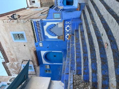 Traditional blue door and arched window facade atop curved stone steps in Chefchaouen.