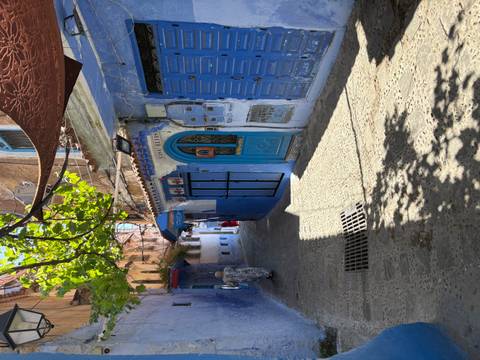 Shaded alley in Chefchaouen with blue doors, patterned awnings and a lone local walking.