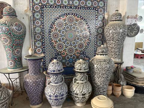 Display of intricately patterned Moroccan pottery vases against a colorful tiled backdrop.