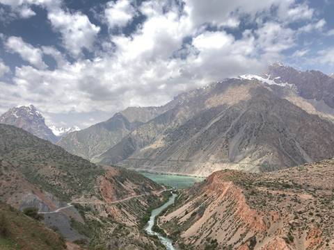 Turquoise lake nestled among steep multicolored mountains under a partly cloudy sky.