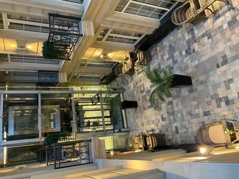Elegant hotel atrium with glass elevator, tiled floor and potted palm.