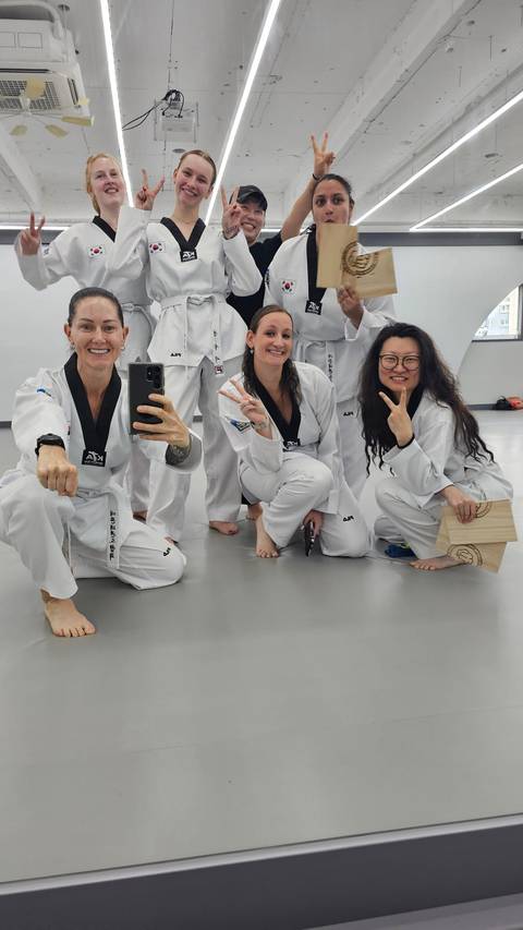 Group of martial-arts students in white doboks smile and pose for a selfie in a taekwondo studio.
