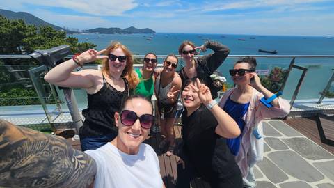 Friends take a cheerful rooftop selfie overlooking the blue sea and distant mountains on a sunny day.