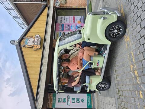 Group of travellers sit in an open-sided electric tuk-tuk outside a rental shop.