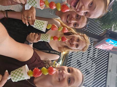 Friends show off colorful fruit skewers at a lively street market.