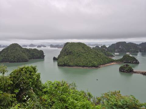 High vantage view of emerald waters and numerous lush limestone islets of Halong Bay under a low cloud ceiling.