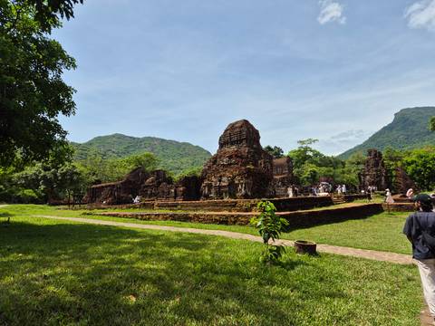 Ancient brick ruins of My Son Sanctuary surrounded by lush green mountains and visitors exploring the site.