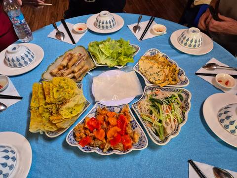 Table set with an array of colorful Vietnamese dishes including pancakes, spring rolls, salads and vegetables.