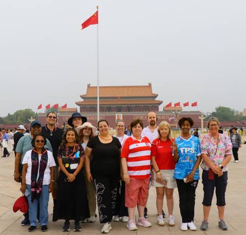 Group tour photo in front of Tiananmen Gate with red flags flying on a hazy Beijing morning.