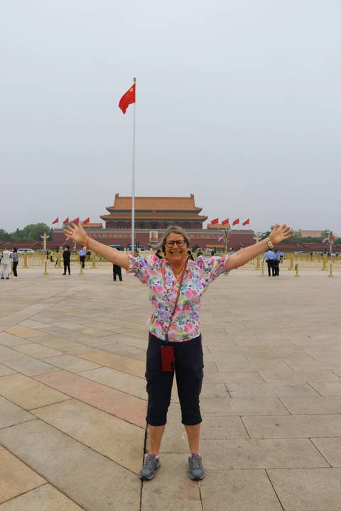 Traveler with arms raised in Tiananmen Square in front of the Forbidden City’s main gate on a hazy day.