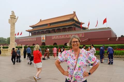 Traveler posing in front of Tiananmen Gate with Mao portrait while visitors and guards disperse around.
