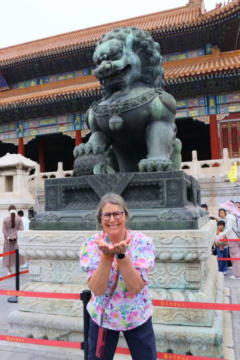 Smiling visitor posing in front of a large bronze guardian lion inside the Forbidden City.