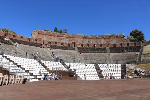 Ancient Greek Theatre of Taormina with stone seating and visitors under blue sky