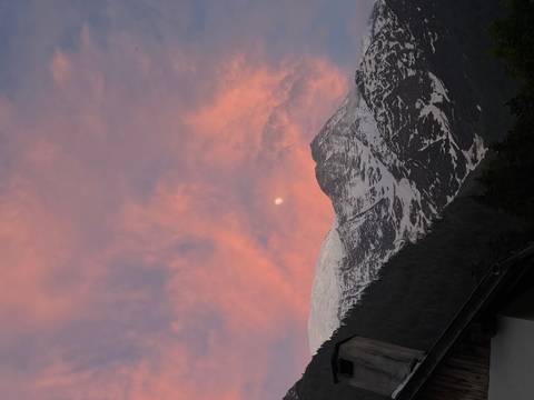 Snowy mountain peak beneath a pink and orange sunset sky with the moon rising.