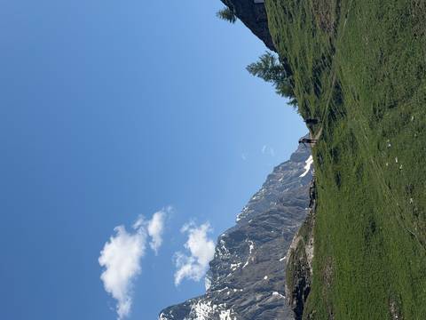 Hikers climbing a grassy alpine slope with rugged mountain cliffs towering nearby.