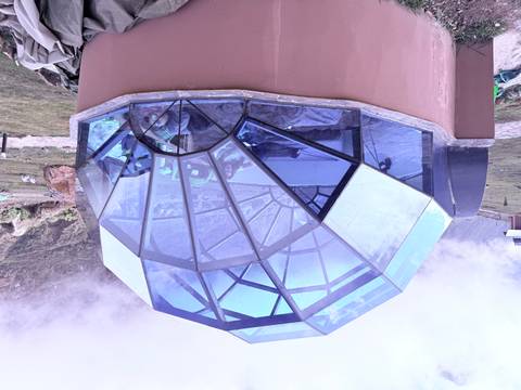 Glass-domed sky camp accommodation with a traveler relaxing inside amid misty mountains.