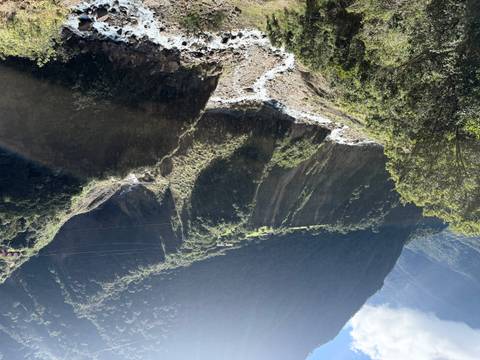 Steep green canyon with a river running through and sun rays filtering over the ridge.