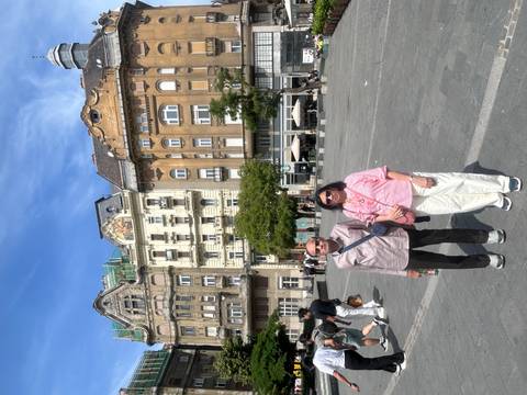 Older couple stands in a European city square with ornate historic buildings behind them.