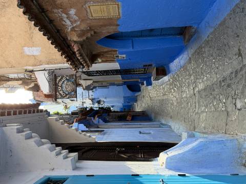 Narrow cobblestone alleyway in Chefchaouen’s blue medina with rustic signage and vivid painted walls.