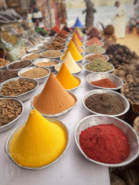 Colorful mounds of spices arranged in metal bowls at an outdoor market