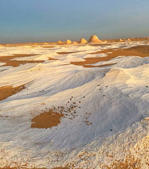Sweeping view of white chalk formations contrasting with orange desert sand at golden hour