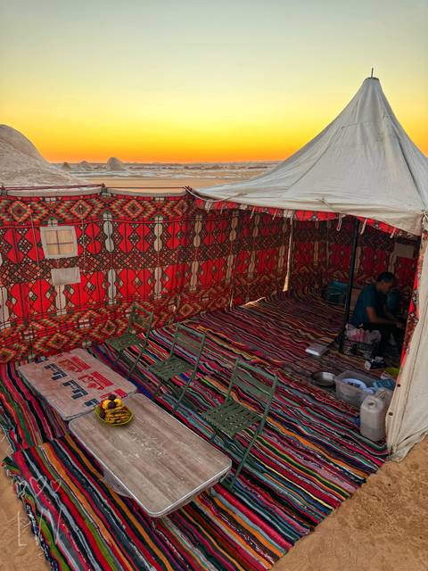 Colorful Bedouin-style tent with patterned fabric walls and low seating, a man preparing supplies