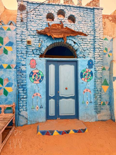 Brightly painted blue doorway with geometric and symbolic motifs on adobe wall