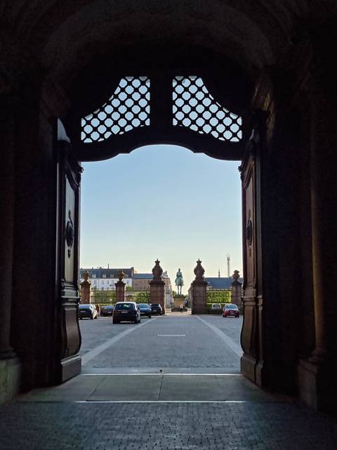 Framed city view through ornate palace gates with an equestrian statue in the distance.