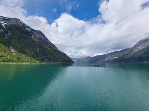 Turquoise fjord flanked by steep green mountains under dramatic clouds.