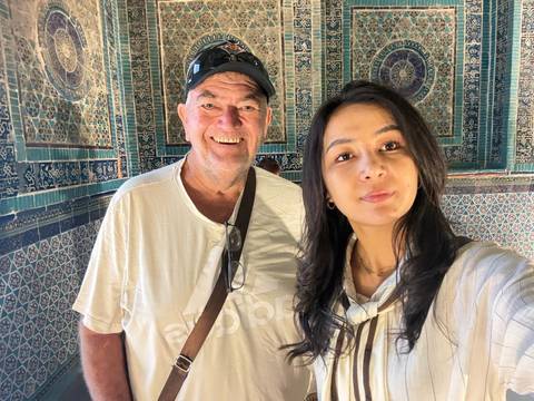 Selfie of an older man and younger woman inside a room covered with intricate blue Islamic tiles