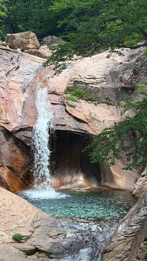 Narrow waterfall plunging down pinkish granite cliff in a forested mountain area