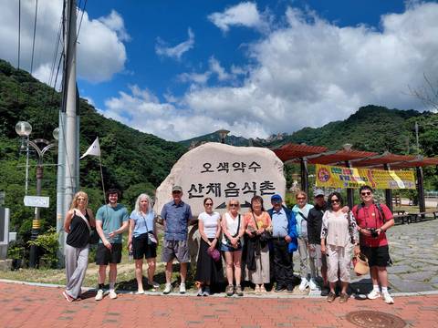Tour group posing in front of a large inscribed stone with green mountains and blue sky behind